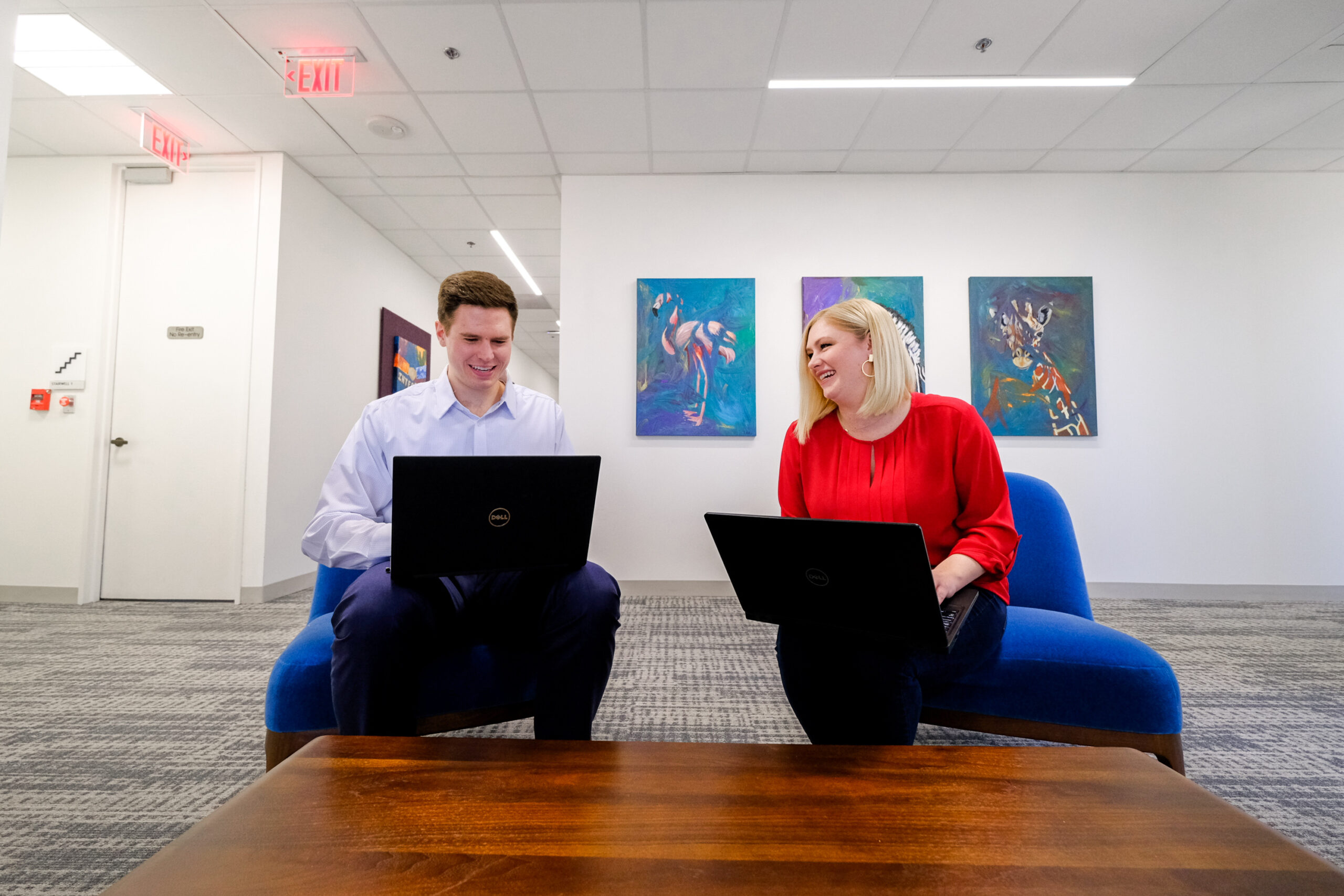 A Caucasian male and Caucasian female sitting in office chairs on laptops