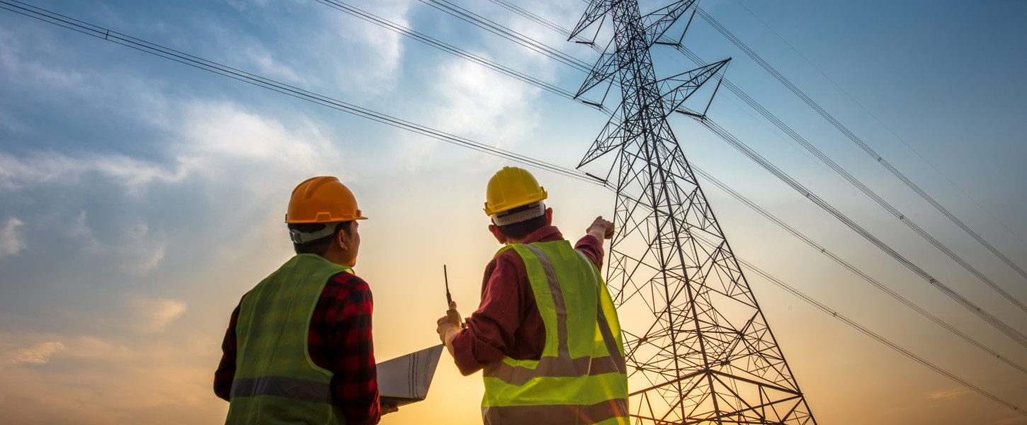 People in construction vests with a computer in front of a transmission tower