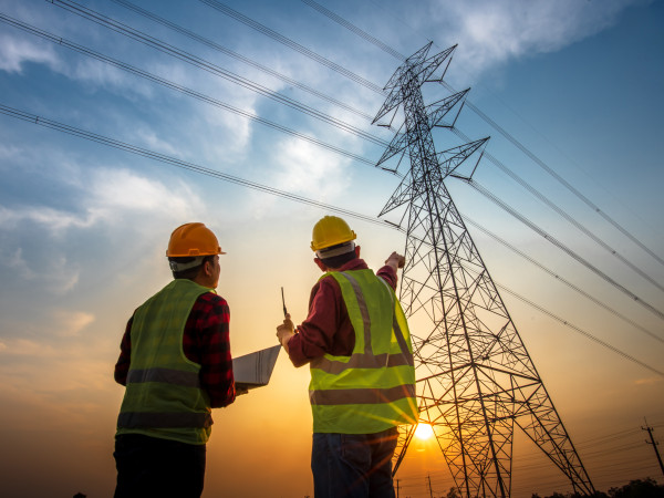 People in construction vests with a computer in front of a transmission tower