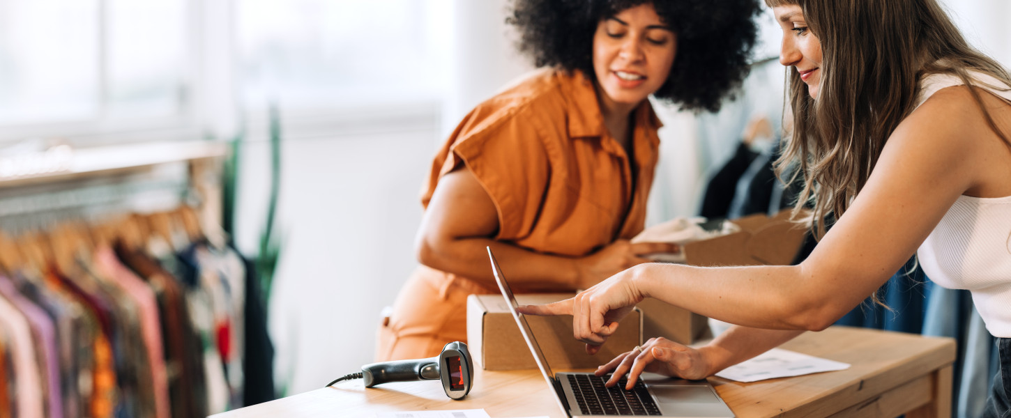 Two women retail employees looking at a laptop and talking