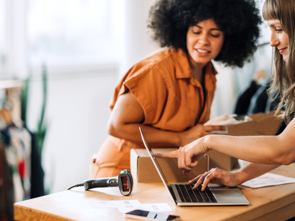 Two women retail employees looking at a laptop and talking
